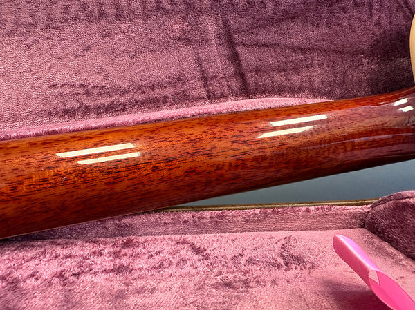 Close-up of glossy wooden guitar neck resting in a pink plush-lined guitar case interior