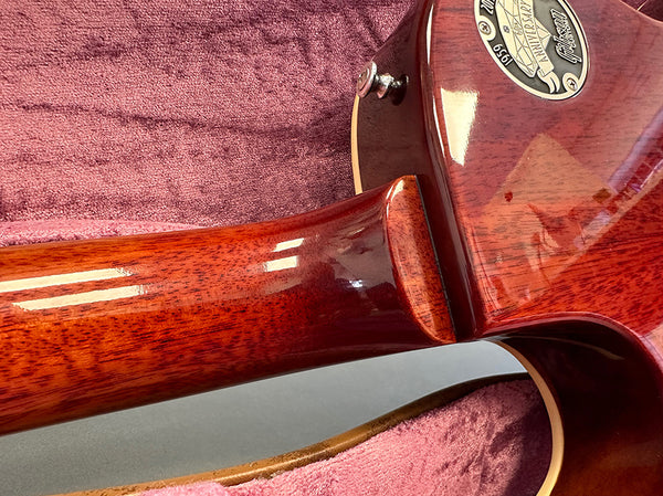 Close-up of Gibson guitar neck joint showing mahogany wood grain and 125th Anniversary 1894-2019 commemorative plaque on guitar body resting in pink plush case lining.