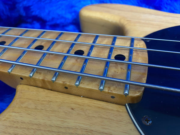 Close-up of natural wood bass guitar neck with metal frets and wound strings against blue background