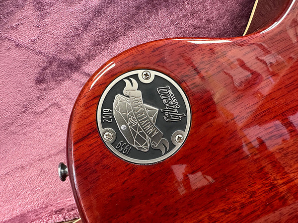 Close-up of Gibson Custom 60th Anniversary 1959 Les Paul guitar commemorative metal badge on polished mahogany back body with pink fabric background