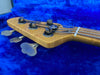 Close-up of a maple wood bass guitar headstock with tuning pegs and strings on a blue plush background