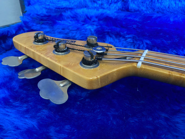 Close-up of a maple wood bass guitar headstock with tuning pegs and strings on a blue plush background