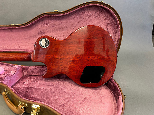 Back view of glossy mahogany electric guitar resting in pink plush lined hard case showing control cavity cover and warranty sticker