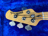 Maple headstock of Purple Bull Music Man Stingray bass guitar with tuning pegs on blue plush background