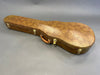 Brown textured hard guitar case with leather handle and gold latches on gray background