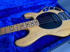Natural wood finish electric bass guitar with black pickguard and maple neck, displayed on blue plush guitar case interior