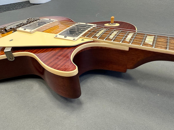 Close-up of sunburst finish electric guitar body with dual humbucker pickups and cream pickguard on gray surface