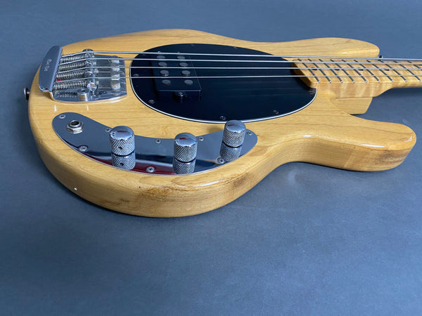 Natural finish electric bass guitar body with black pickguard and chrome control knobs on gray background