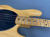 Close-up of natural wood electric bass guitar body and maple fretboard with black pickguard and metal frets on gray background