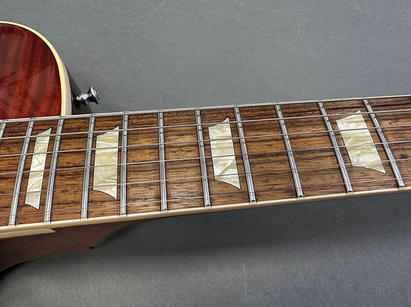 Close-up of electric guitar rosewood fretboard with trapezoid pearloid inlays and metal frets on dark gray background
