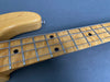 Close-up of maple fretboard and neck of a four-string electric bass guitar with dot inlays and metal frets on a dark surface background