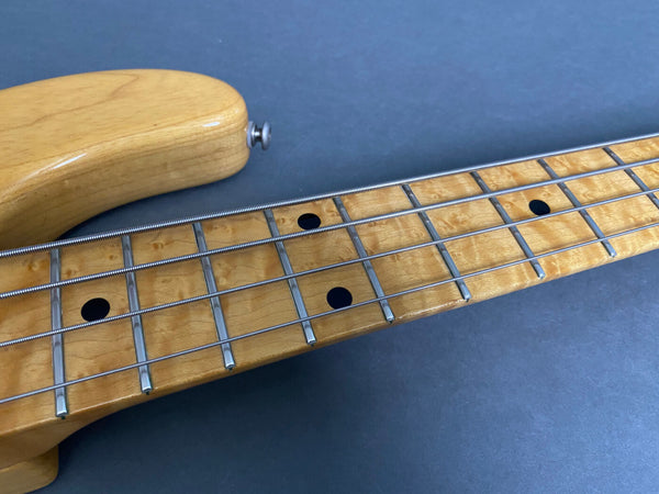 Close-up of maple fretboard and neck of a four-string electric bass guitar with dot inlays and metal frets on a dark surface background