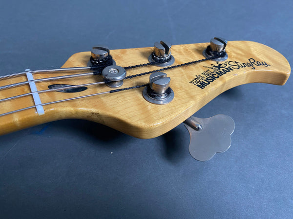 Close-up of Ernie Ball Music Man StingRay bass guitar headstock with tuning pegs and strings on a dark background