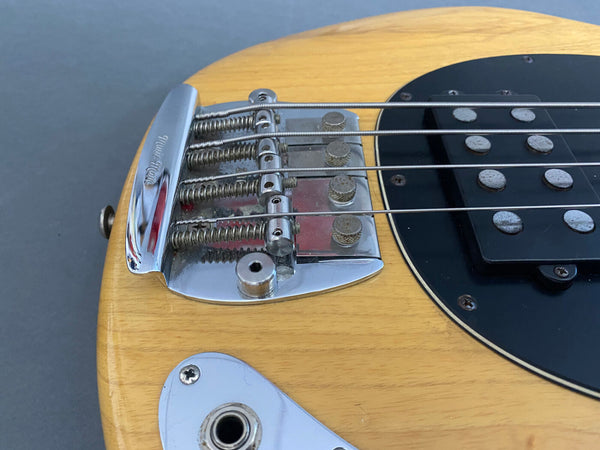 Close-up of natural wood electric bass guitar bridge, strings, and black pickup with chrome hardware and input jack