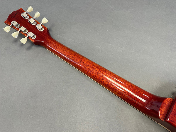 Back of guitar neck with six tuning pegs and glossy reddish wood finish on gray background