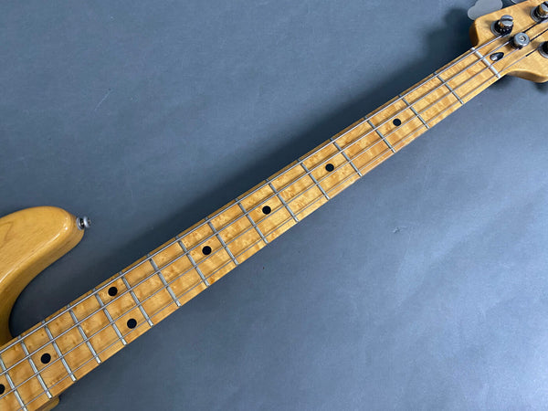 Close-up of maple fretboard on electric bass guitar with black dot inlays and chrome tuning pegs against gray background