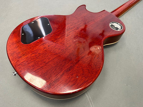 Back of glossy cherry red electric guitar body showing wood grain and black plastic control cavity cover.