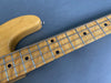 Close-up of maple fingerboard and neck on natural wood electric bass guitar with black dot inlays and metal frets against gray background