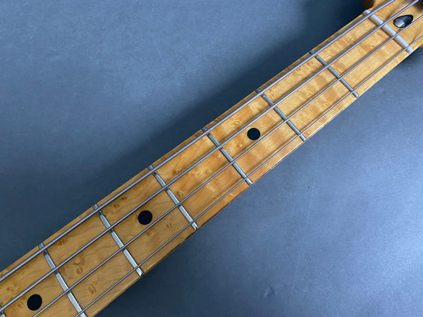 Close-up of maple fretboard with black dot inlays and metal frets on electric bass guitar strings against gray background
