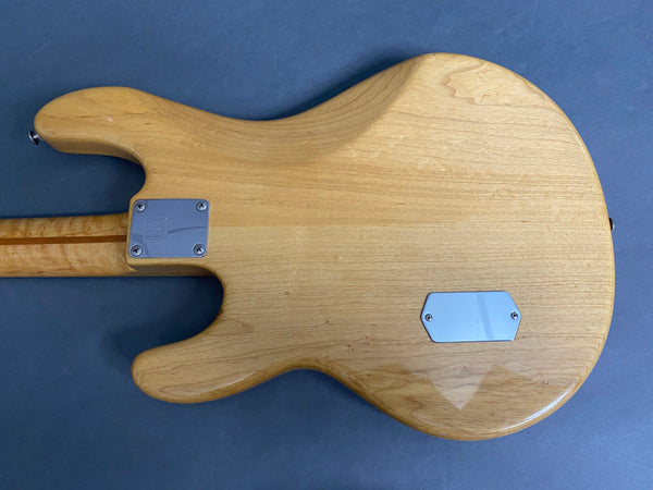 Back side of natural wood electric guitar body with metal neck plate and back control cover on gray surface