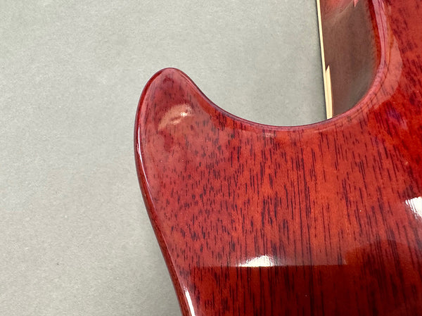Close-up of red stained wood grain on electric guitar body corner with glossy finish at Coffee House Guitars