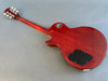 Back view of red solid body electric guitar with mahogany wood finish and black control cavity cover on a gray surface