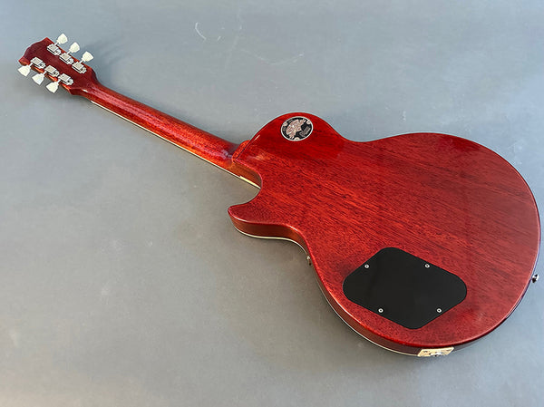 Back view of red solid body electric guitar with mahogany wood finish and black control cavity cover on a gray surface