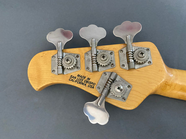 Close-up of vintage bass guitar headstock with four tuning keys, made in San Luis Obispo, California, USA, showing natural wood finish and metal tuning gears
