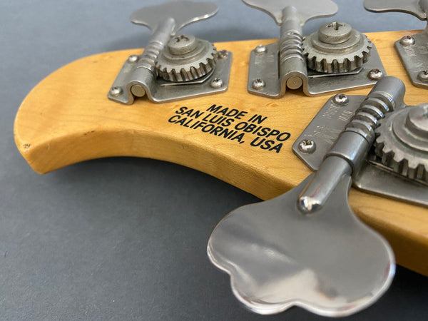 Close-up of vintage bass guitar tuning pegs with "Made in San Luis Obispo California USA" stamp on wooden headstock