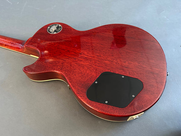 Back view of red mahogany electric guitar body with black control cavity cover and gold hardware on gray surface, Coffee House Guitars product listing image.