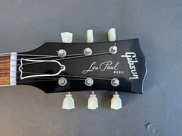 Close-up of Gibson Les Paul model black guitar headstock with tuning pegs and strings on gray background