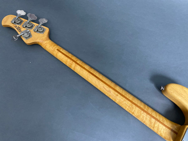 Back view of maple neck and tuning pegs on electric bass guitar with "Made in Corona, California" stamp on headstock