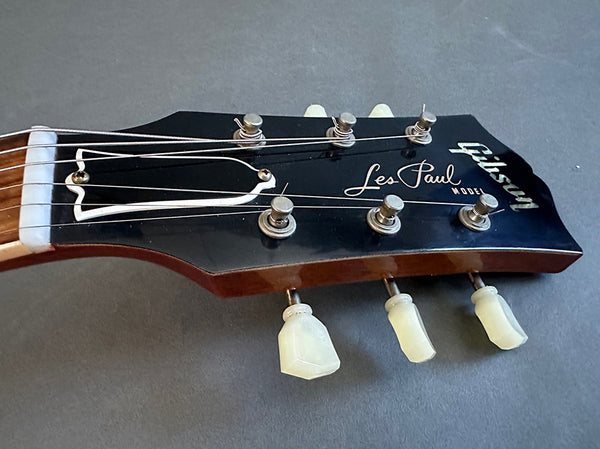 Close-up of Gibson Les Paul Model guitar headstock with tuning pegs and strings against gray background