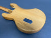 Back of natural finish electric guitar body with metal neck plate and control cavity cover on gray background