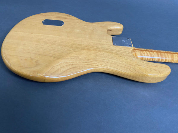 Back view of natural wood electric guitar body with metal neck plate on dark surface