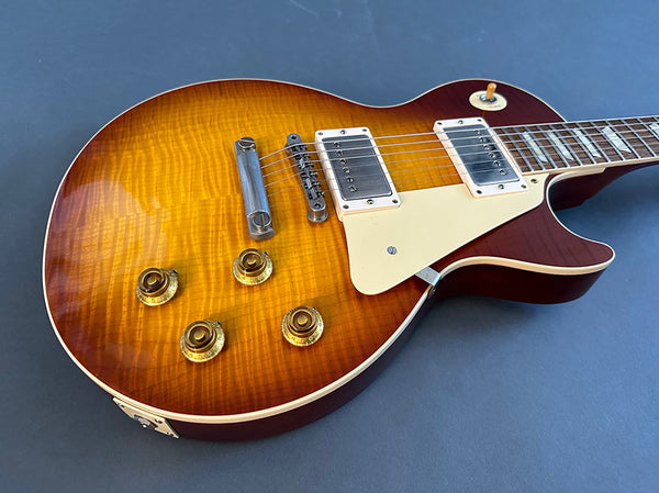 Sunburst electric guitar with dual humbucker pickups and four gold control knobs on gray background, close-up view of body and neck.