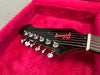 Close-up of black electric guitar headstock with chrome tuning pegs inside red plush guitar case, featuring Inspyre logo on headstock