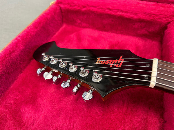 Close-up of black electric guitar headstock with chrome tuning pegs inside red plush guitar case, featuring Inspyre logo on headstock