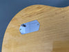 Close-up of natural wood finish electric guitar back with metal control cavity cover plate and two screws against blue background