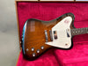 Sunburst electric guitar with white pickguard and chrome bridge resting in red velvet-lined guitar case