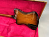 Back side view of sunburst electric guitar body resting in red plush-lined hard case