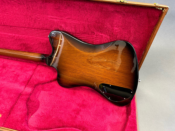 Back side view of sunburst electric guitar body resting in red plush-lined hard case