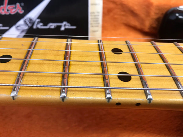 Close-up of vintage Fender maple guitar neck and fretboard with steel strings and dot inlays, resting on orange fabric case interior