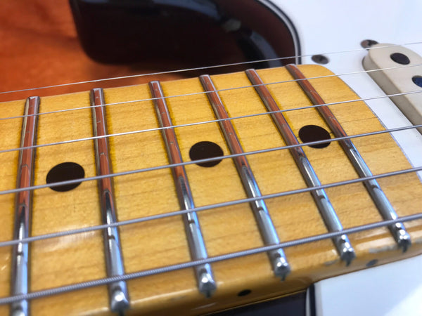 Close-up of electric guitar maple fretboard with metal frets and strings showing dot inlays and white pickguard