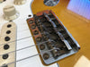 Close-up of vintage electric guitar bridge and saddles with rusted screws, showing volume knob and white pickup rings on yellow guitar body