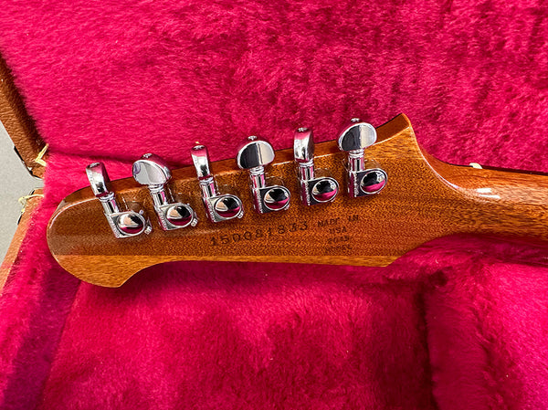 Close-up of guitar headstock back showing six chrome tuning pegs on mahogany wood with serial number and "Made in USA" stamp, resting on red plush lining inside guitar case