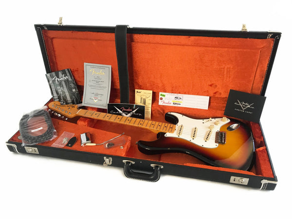 Fender Stratocaster electric guitar in sunburst finish with maple neck and fretboard inside black hardshell case with orange plush interior, including Fender Certificate of Authenticity, accessories, and documentation