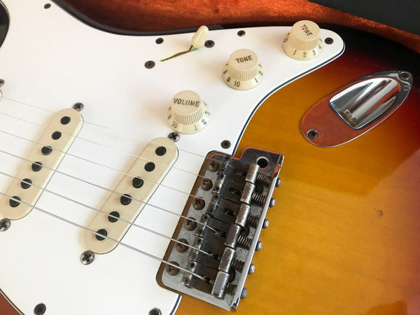 Close-up of vintage electric guitar bridge, pickups, and control knobs for volume and tone on sunburst finish body with white pickguard