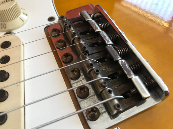 Close-up of vintage electric guitar bridge and strings with white pickguard and tone control knob on amber body