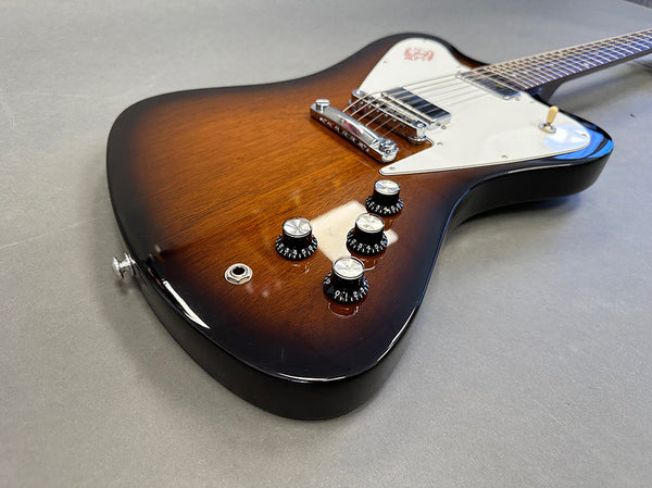 Electric guitar with sunburst finish, white pickguard, chrome bridge, and four black control knobs on gray background